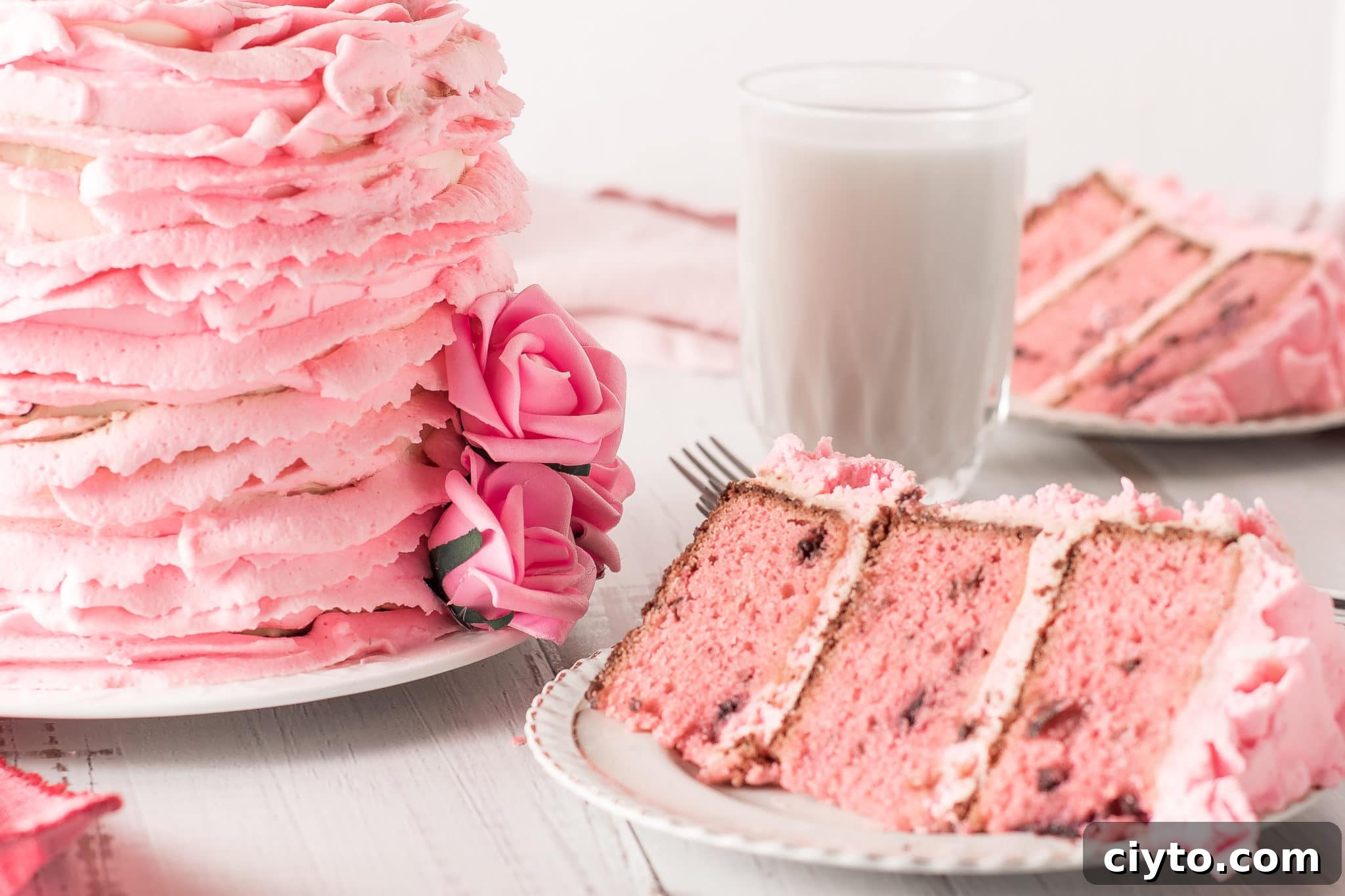 A pink ruffled cherry chip cake with slices laid out on a white wooden table top