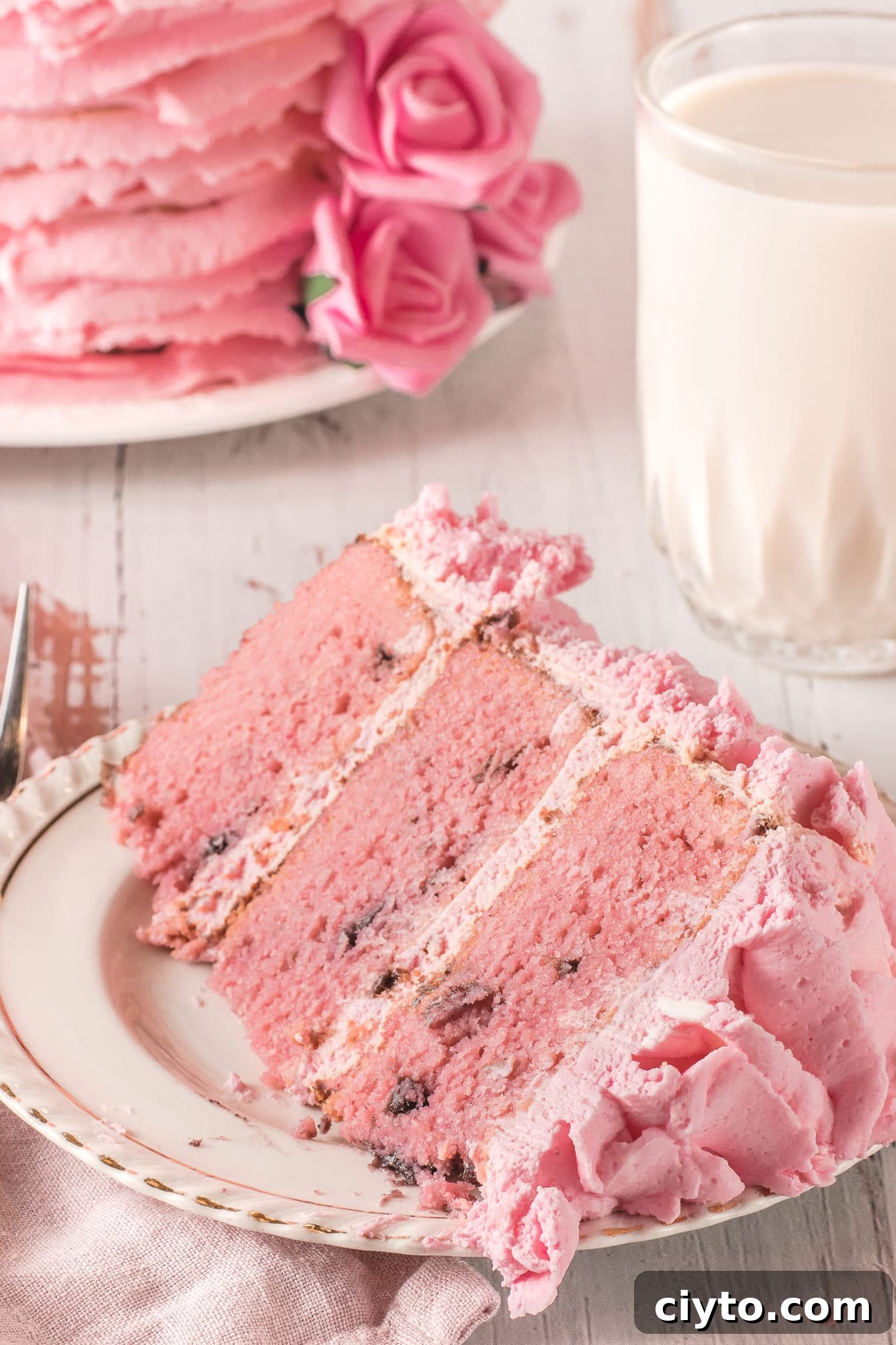 A big slice of pretty pink low carb cherry chip cake on a cream colored plate with gold rim.