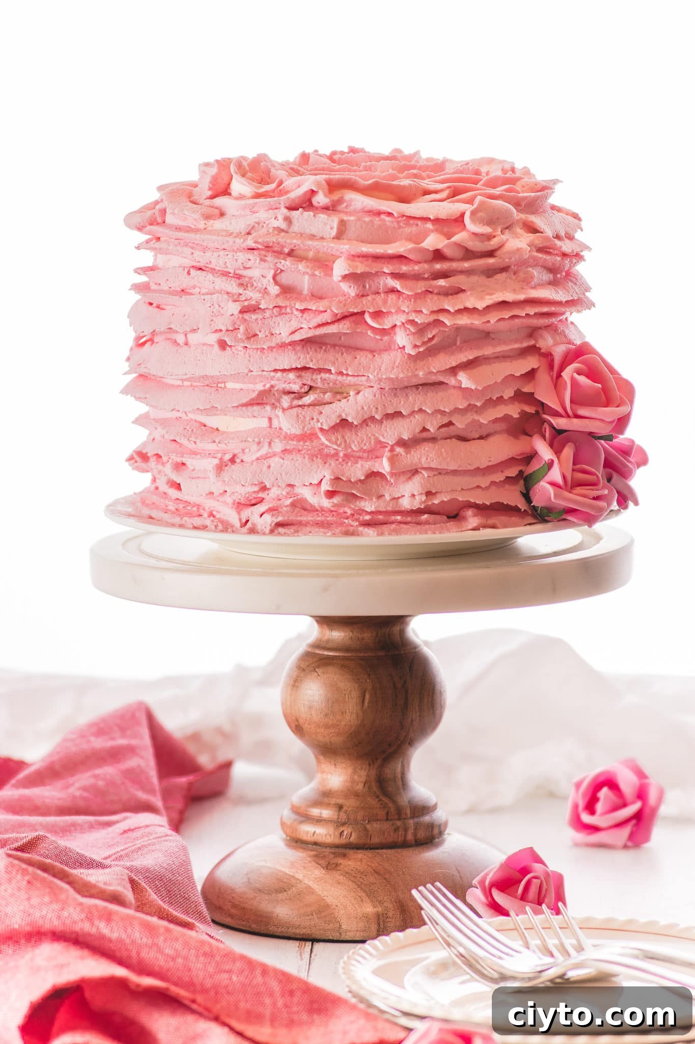 A pink ruffled cake on a marble and wooden cake against a bright white tabletop and background