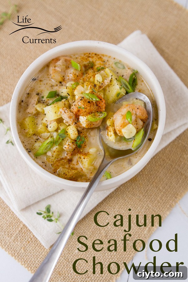 A bowl of Cajun seafood chowder in a white bowl with shrimp, potatoes, corn, and green onions, and a spoon on a napkin 