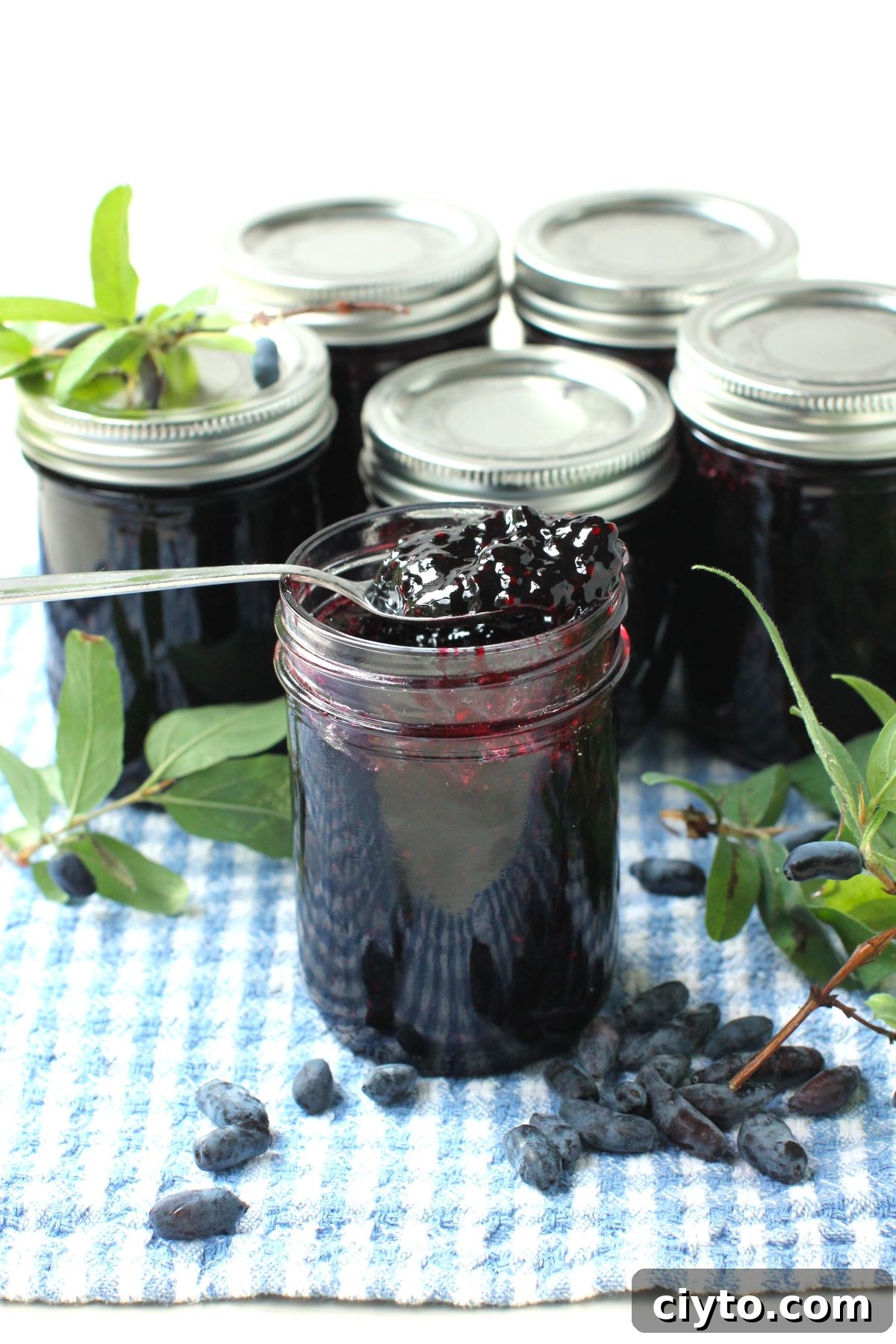 jar of haskap jam with spoonful of jam propped on top, berries on towel, jars of jam in background