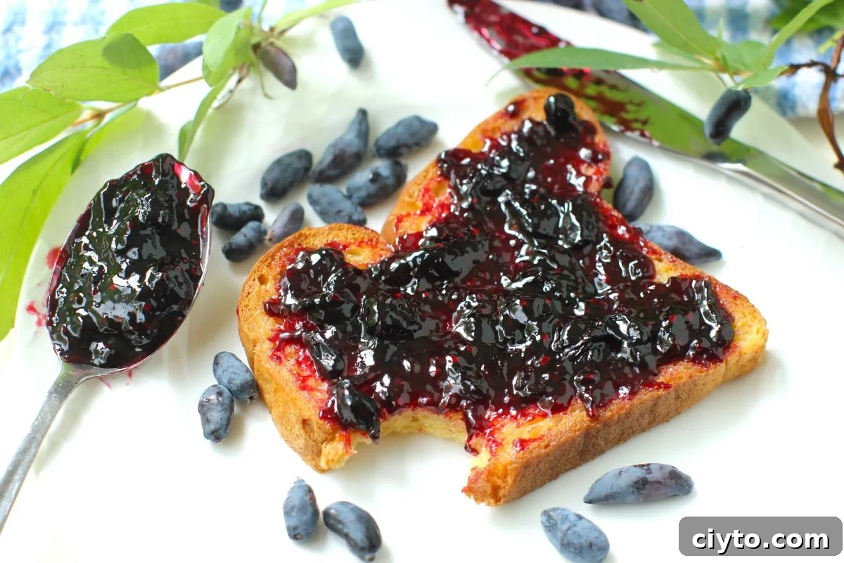 slice of bread spread with honeyberry jam on plate, haskaps on plate, spoonful of jam beside