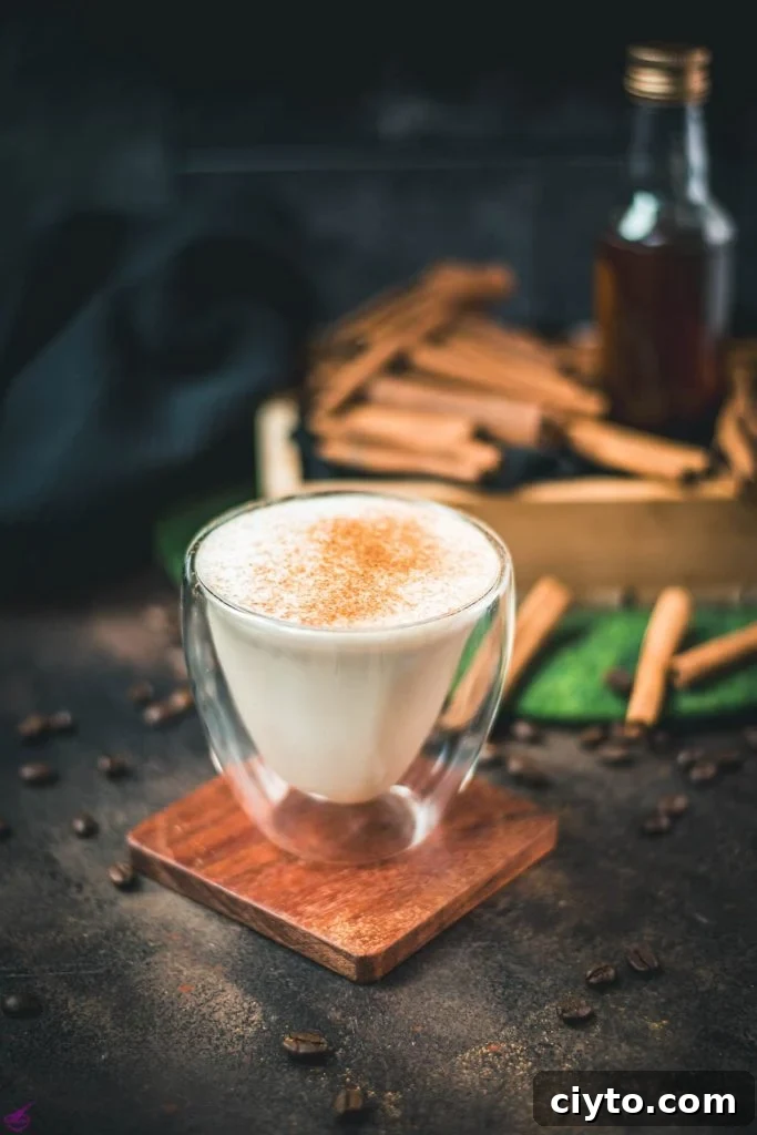 Gorgeous cinnamon dolce latte, dusted with ground cinnamon. Placed on wooden coaster with cinnamon sticks in the background.