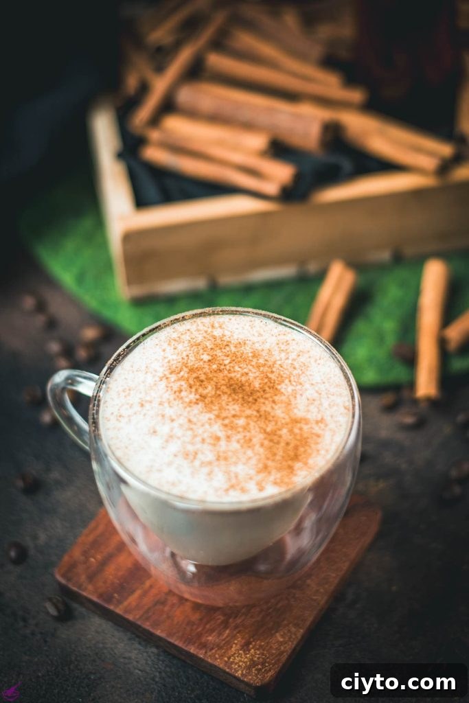 Gorgeous cinnamon dolce latte, dusted with ground cinnamon. Placed on wooden coaster with cinnamon sticks in the background.