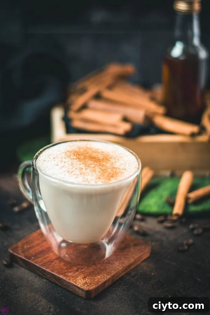 Gorgeous cinnamon dolce latte, dusted with ground cinnamon. Placed on wooden coaster with cinnamon sticks in the background.