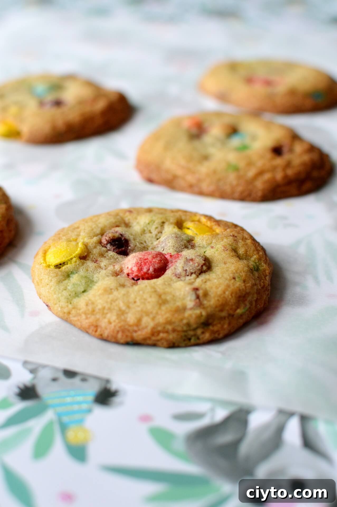 Five gluten free M&M cookies laying on a piece of parchment paper. 