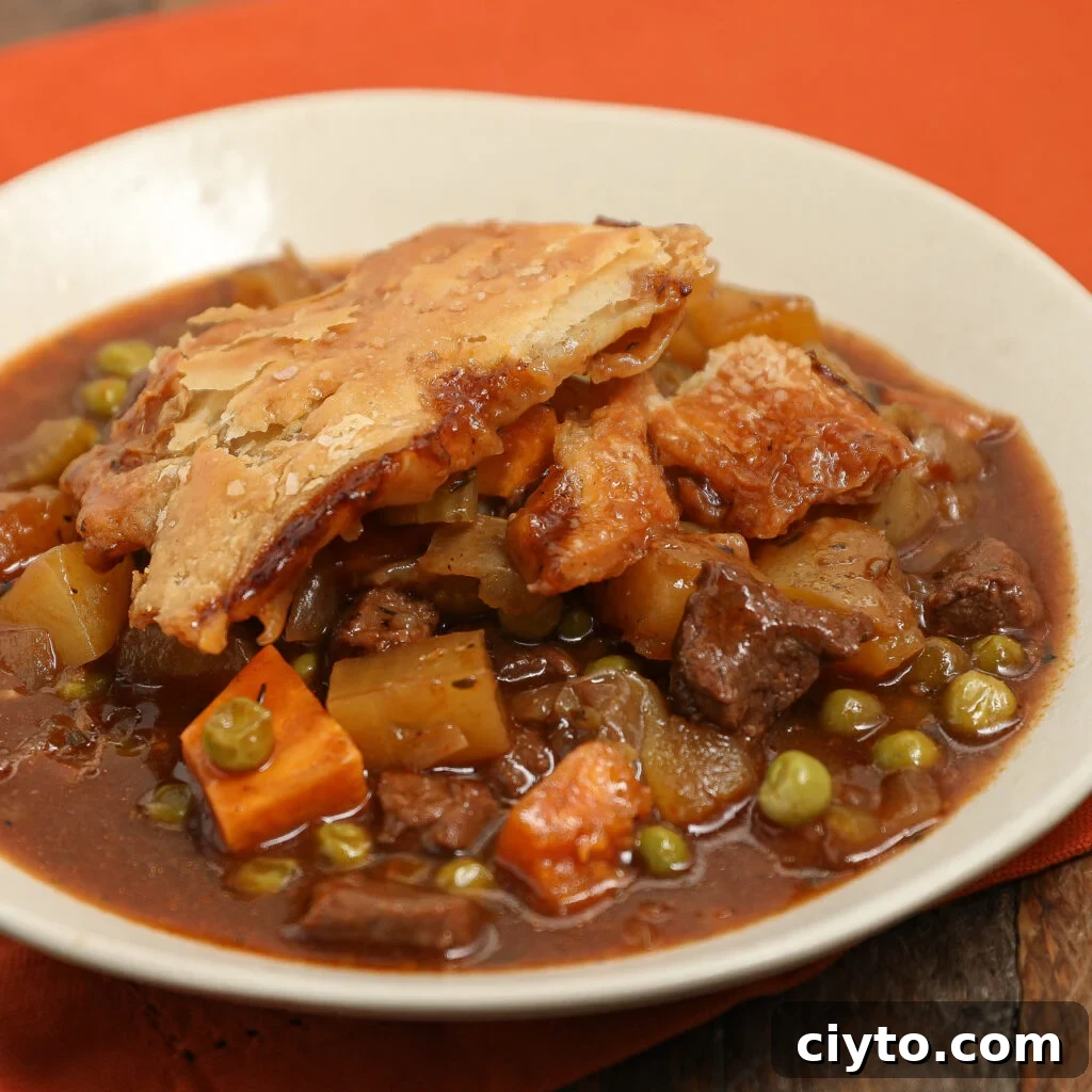 A plate of beef Guinness pot pie with golden, flaky crust on top, filled with chunks of beef, potatoes, carrots, peas, and rich brown gravy, served on a white dish with an orange background.