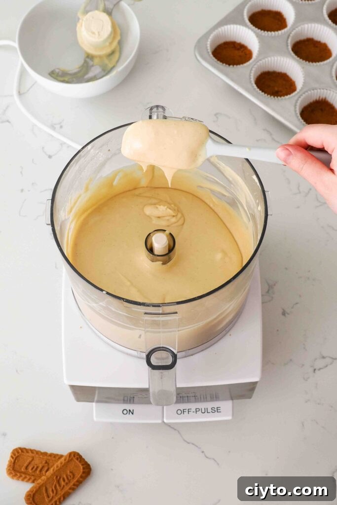 Mini Biscoff Cheesecakes Recipe with Cookie Butter Crust 11 A spatula holds up Biscoff cheesecake batter over a food processor bowl.