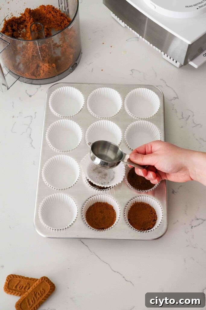 Mini Biscoff Cheesecakes Recipe with Cookie Butter Crust 7 A hand uses a measuring cup to flatten cookie crusts in a muffin pan.