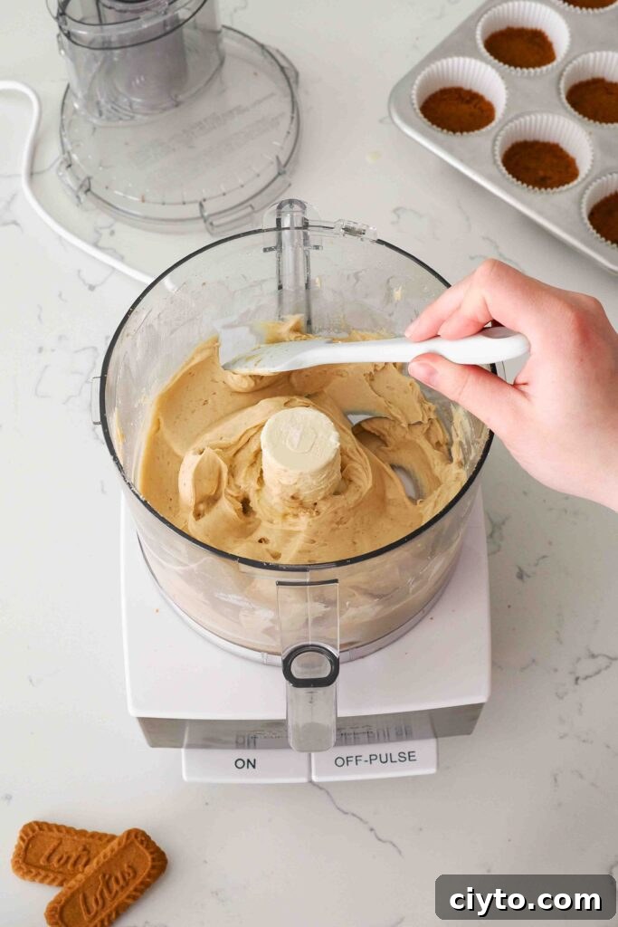 Mini Biscoff Cheesecakes Recipe with Cookie Butter Crust 9 A spatula scrapes down the side of a food processor bowl with Biscoff cheesecake filling on the sides.