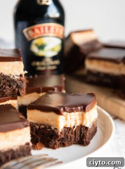 baileys brownie with a bite showing layers of brownie, frosting and ganache on plate with more brownies