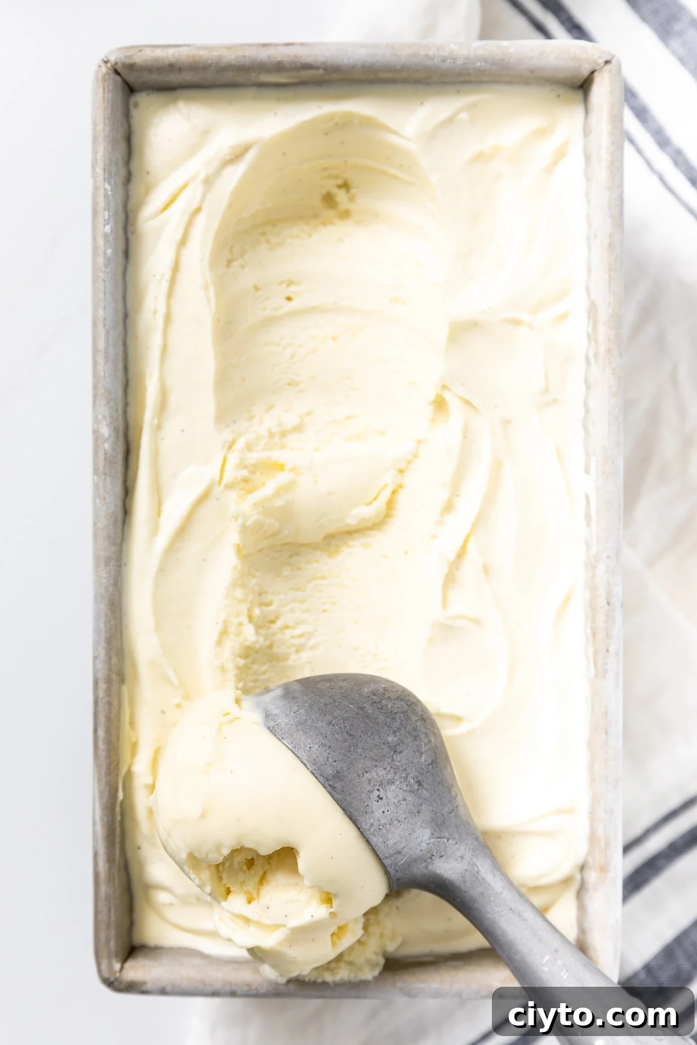Creamy Vanilla Ice Cream Recipe with Real Vanilla Beans 3 Close up view of ice cream scoop scooping vanilla ice cream from silver container in which it was frozen