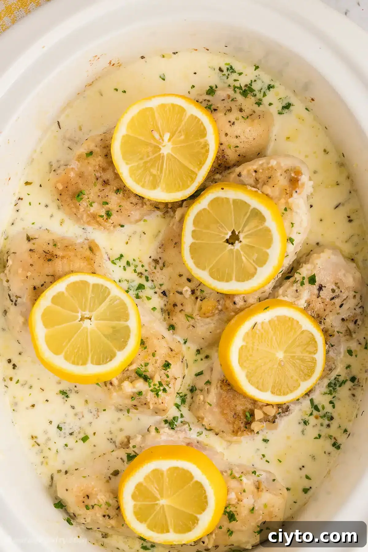 A white slow cooker filled with creamy lemon chicken.