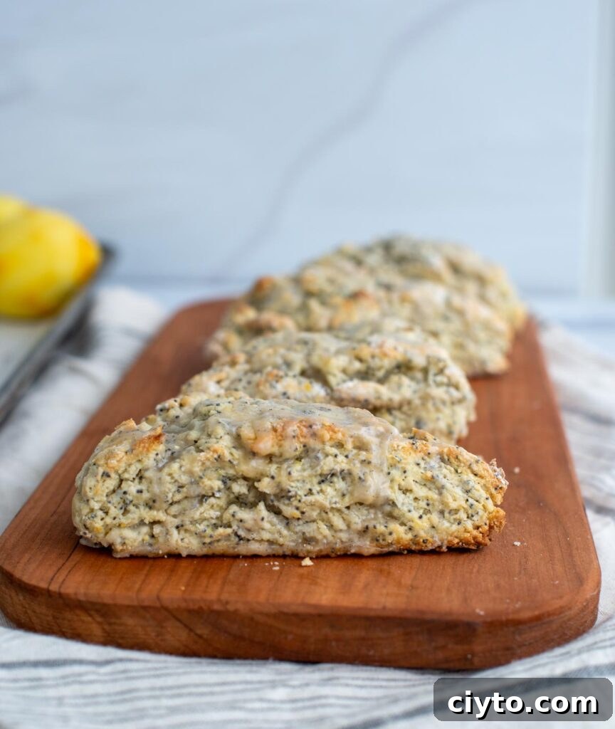 Lemon Poppy Seed Sourdough Scones Recipe 9 A row of finished sourdough scones sits on a serving tray with glaze drizzled on top of them.