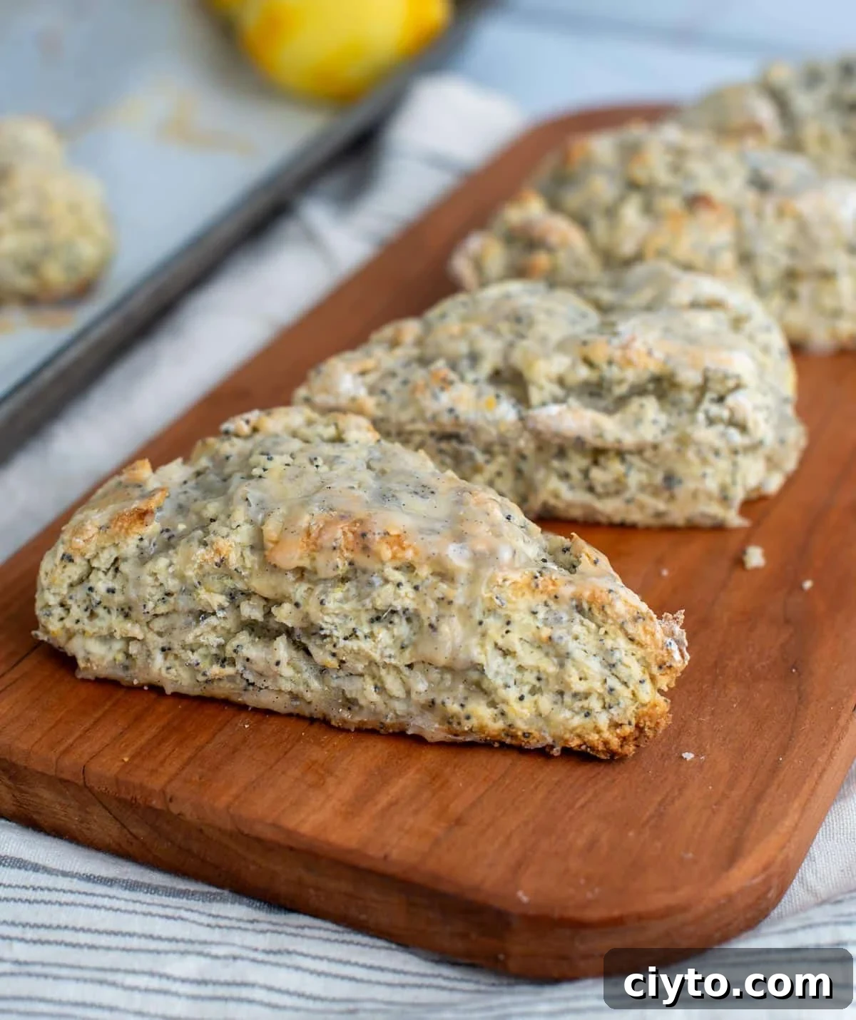 Lemon Poppy Seed Sourdough Scones Recipe 10 A row of sourdough scones topped with sweet glaze are baked and lined up on a platter on the counter.