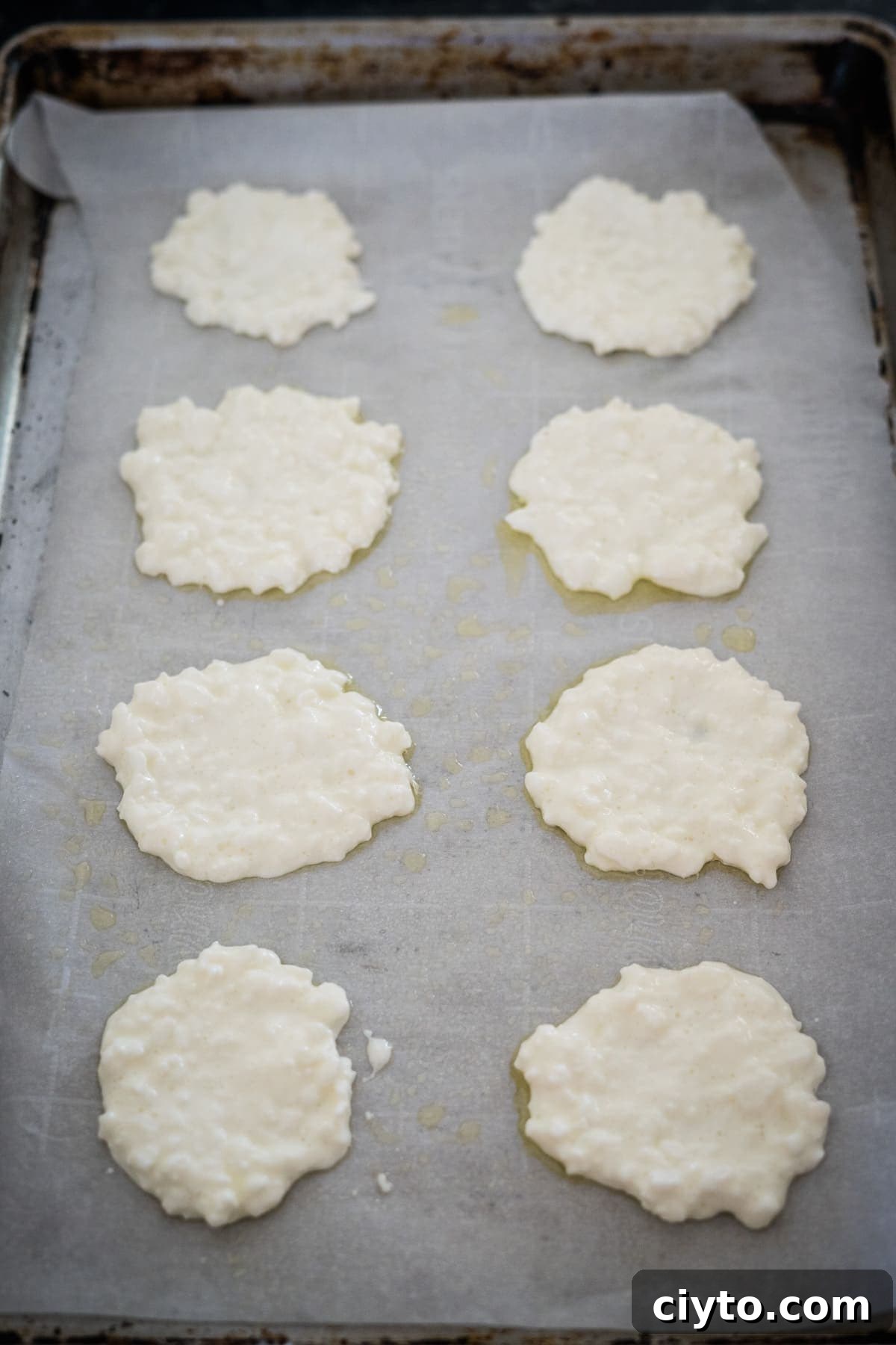 A baking sheet is lined with parchment paper and topped with eight dollops of uncooked cottage cheese.