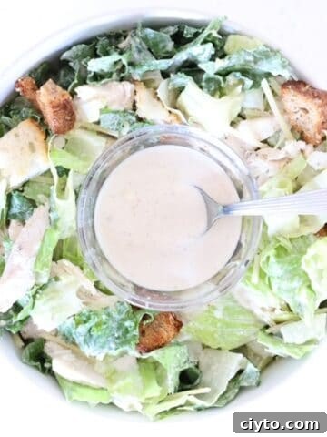 One bowl of Caesar salad with a small glass bowl of Caesar dressing with a spoon in the center.