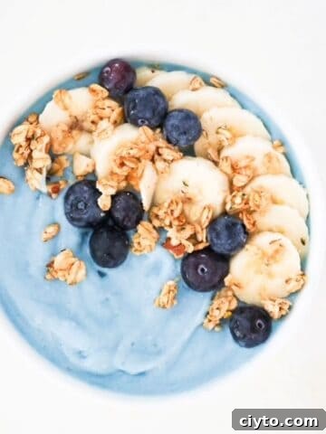 Blue smoothie bowl topped with sliced banana, blueberries, and granola.