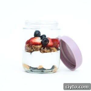 One Greek yogurt parfait with fresh berries in a glass jar with the lid off and leaning on the side of the jar.