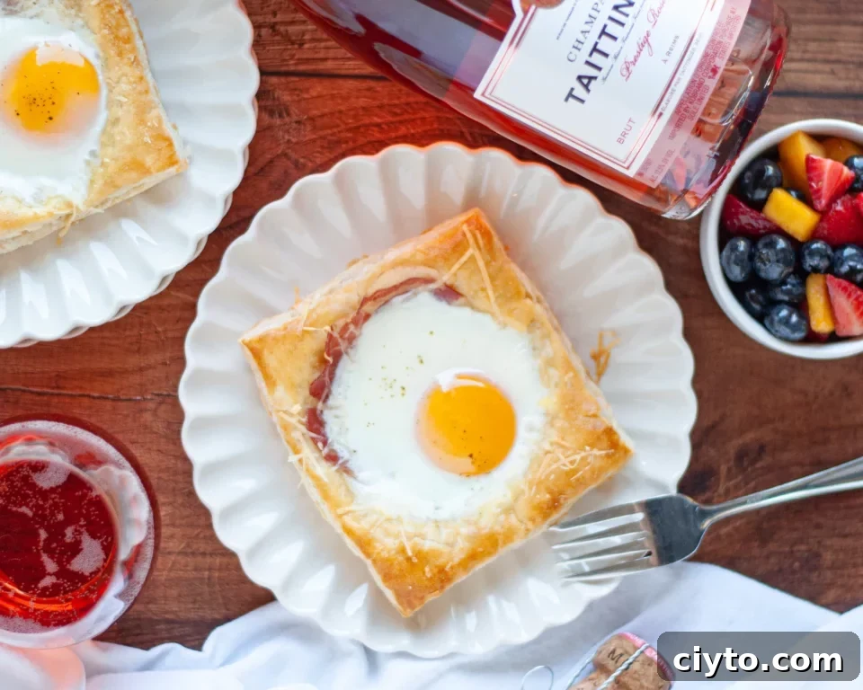 Eggs Benedict served on a white plate with a runny yolk, alongside berries and rosé wine.