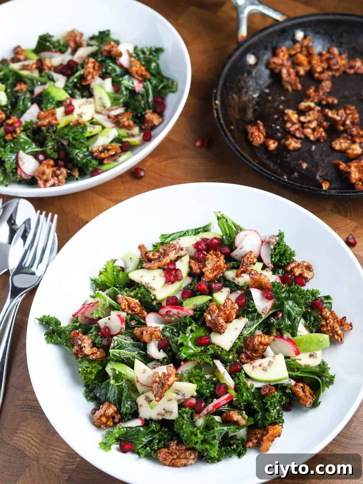 Kale and Apple Salad with Maple-Candied Walnuts 2 Portrait photo of two bowls of kale and apple salad with a small pan of caramelised walnuts in the background.