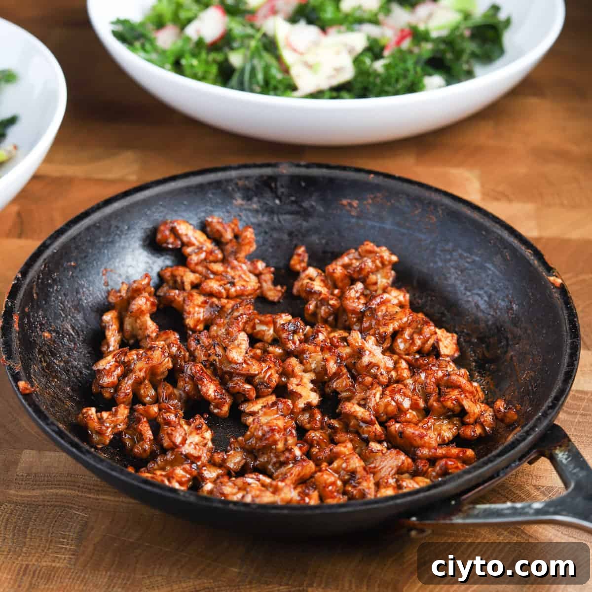 Kale and Apple Salad with Maple-Candied Walnuts 5 Photo of a small pan of caramelised walnuts with bowls of salad in the background.