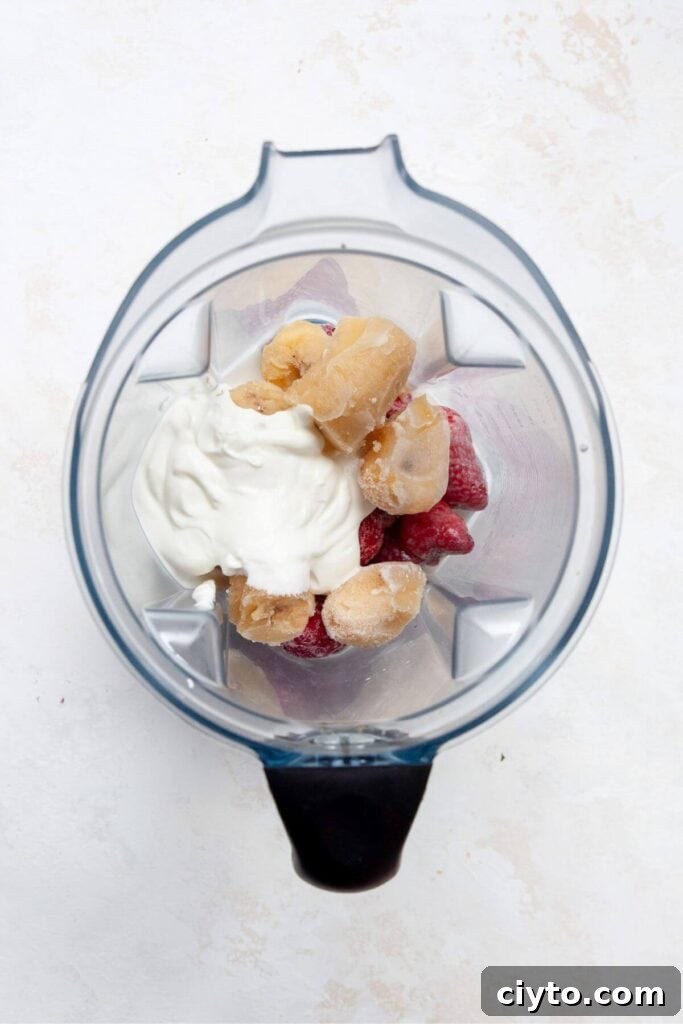 Frozen strawberries, banana, Greek yogurt, and milk in a blender before blending for smoothie bowl