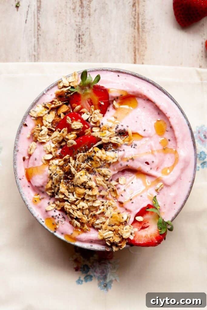 healthy strawberry smoothie bowl topped with crunchy granola and a drizzle of honey