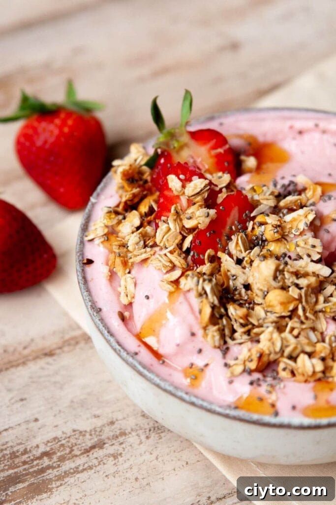 Thick Greek yogurt strawberry smoothie bowl topped with fresh fruit and granola