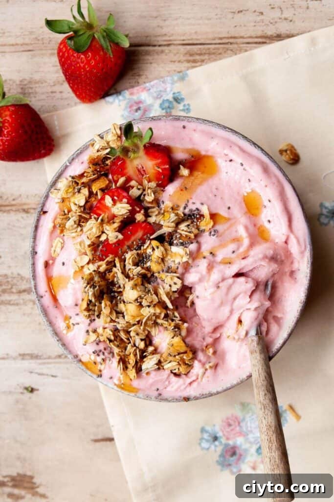 Creamy strawberry smoothie bowl topped with granola, chia seeds, honey drizzle, and fresh strawberries
