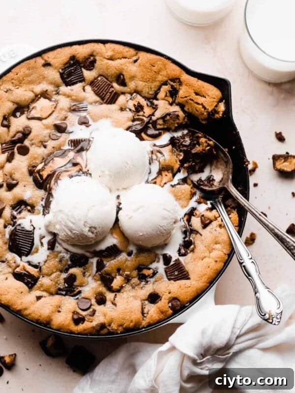 A peanut butter cup and chocolate chip skillet cookie, with scoops of vanilla ice cream on top, and spoons digging in.