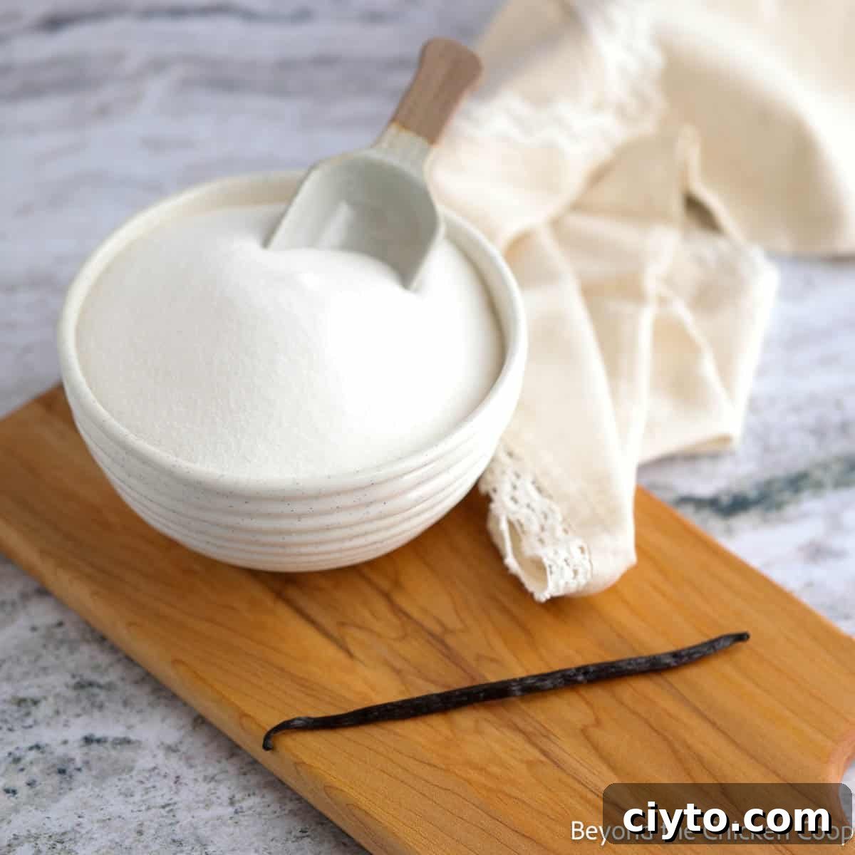 A bowl of sugar and a whole vanilla bean on a wooden board.