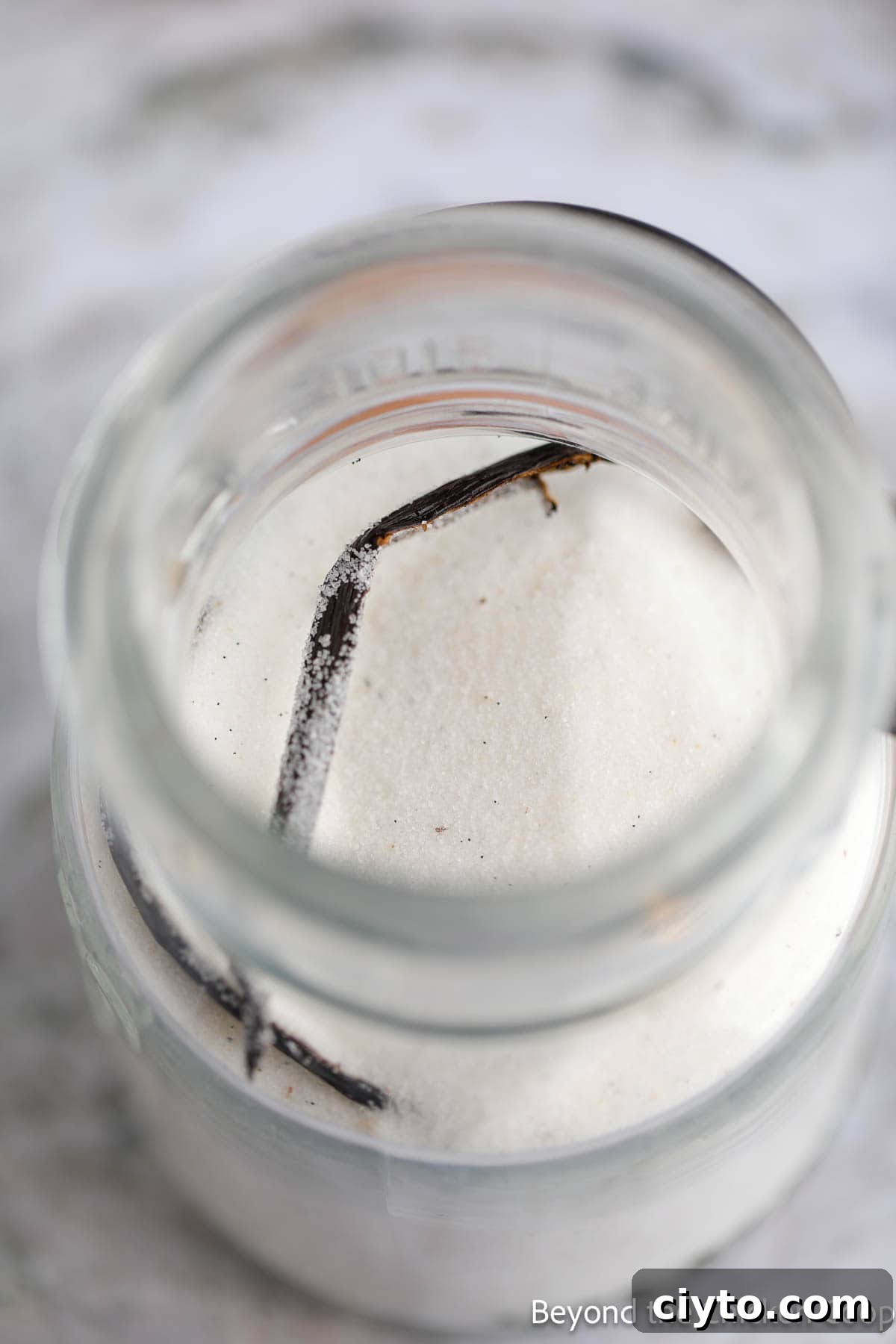 Adding sugar and a vanilla bean half to a glass jar.