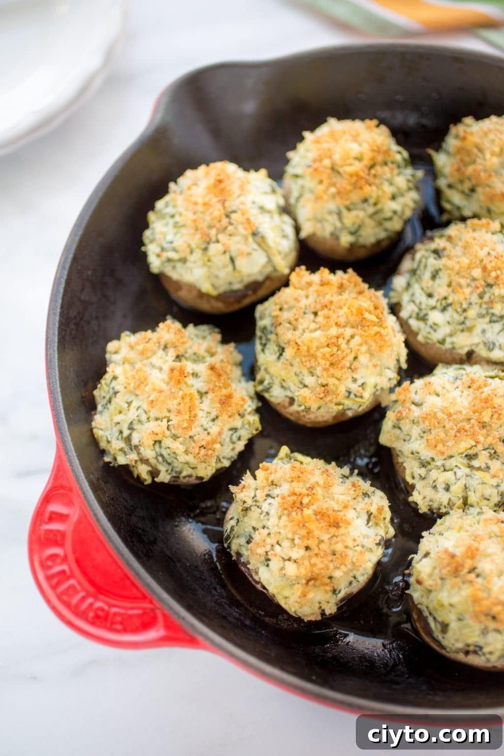 Crumb-topped baked spinach and artichoke stuffed mushrooms in an enameled cast iron skillet.