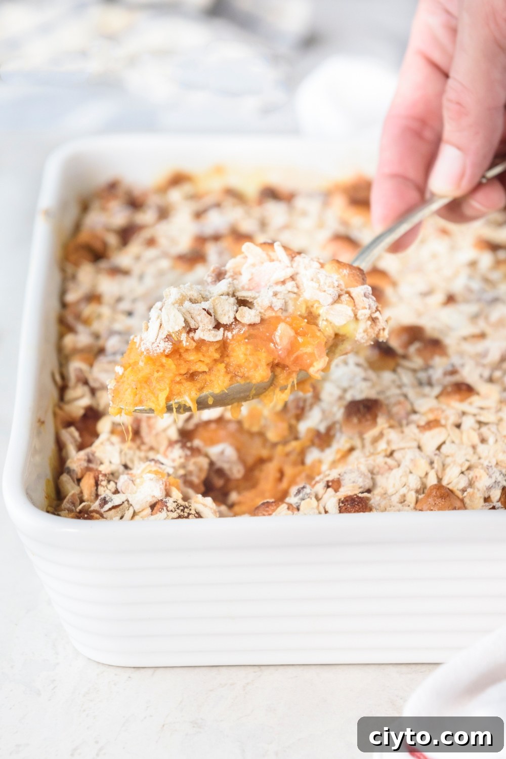Copycat Boston Market Sweet Potato Casserole Recipe 2 Someone is scooping sweet potato casserole out of a white casserole dish with a spoon.