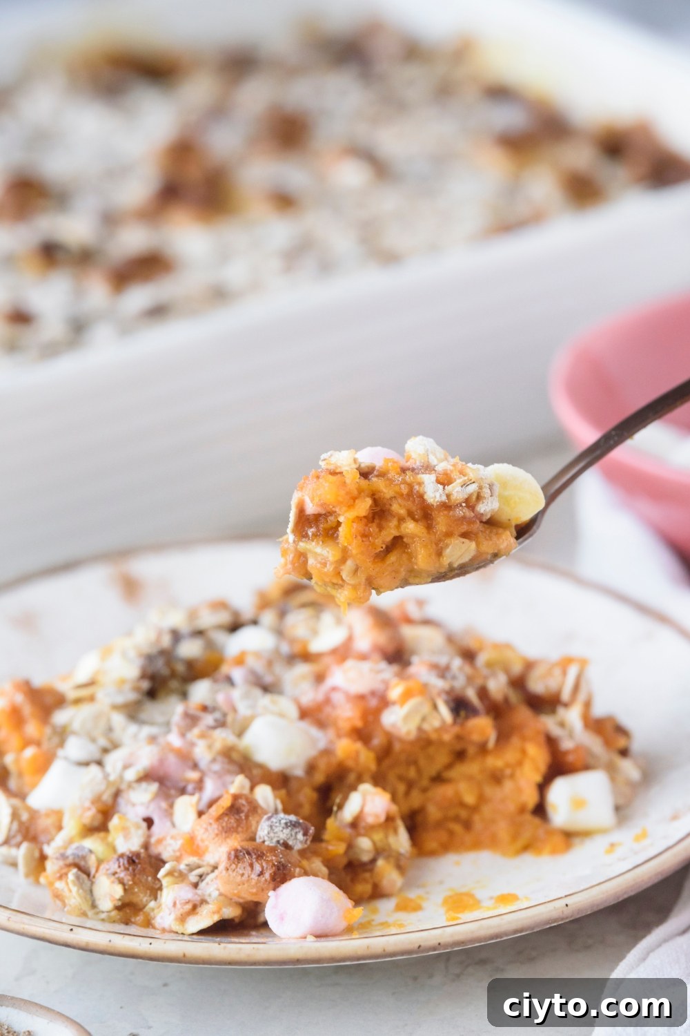 Copycat Boston Market Sweet Potato Casserole Recipe 12 Someone lifting a spoonful of sweet potato casserole from a white plate. A full casserole dish is in the background.