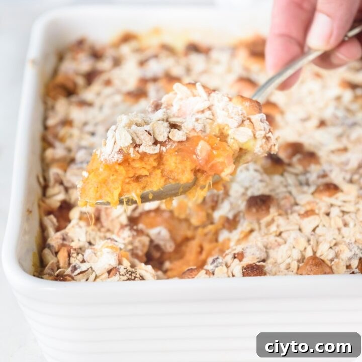 Someone is scooping sweet potato casserole out of a white casserole dish with a spoon.
