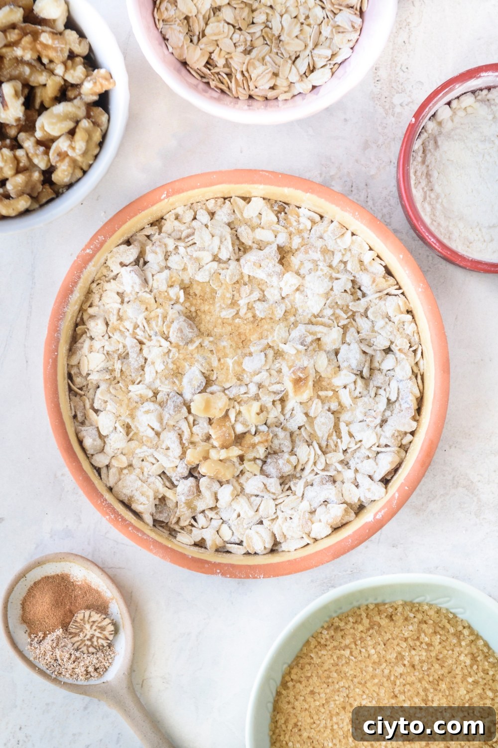 Copycat Boston Market Sweet Potato Casserole Recipe 9 An orange bowl full of oats, walnuts, cinnamon, and sugar. Small bowls of walnuts, oats, flour, brown sugar, and spices surround the bowl.