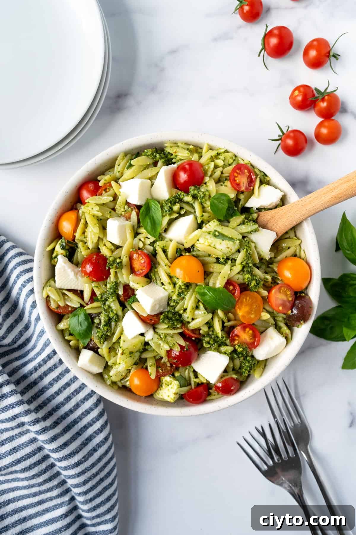 Pesto Orzo Salad in a white bowl with a wooden spoon.