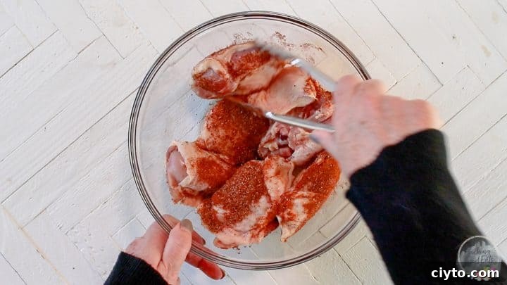 Coating the chicken thighs in dry rub in a class glass bowl.