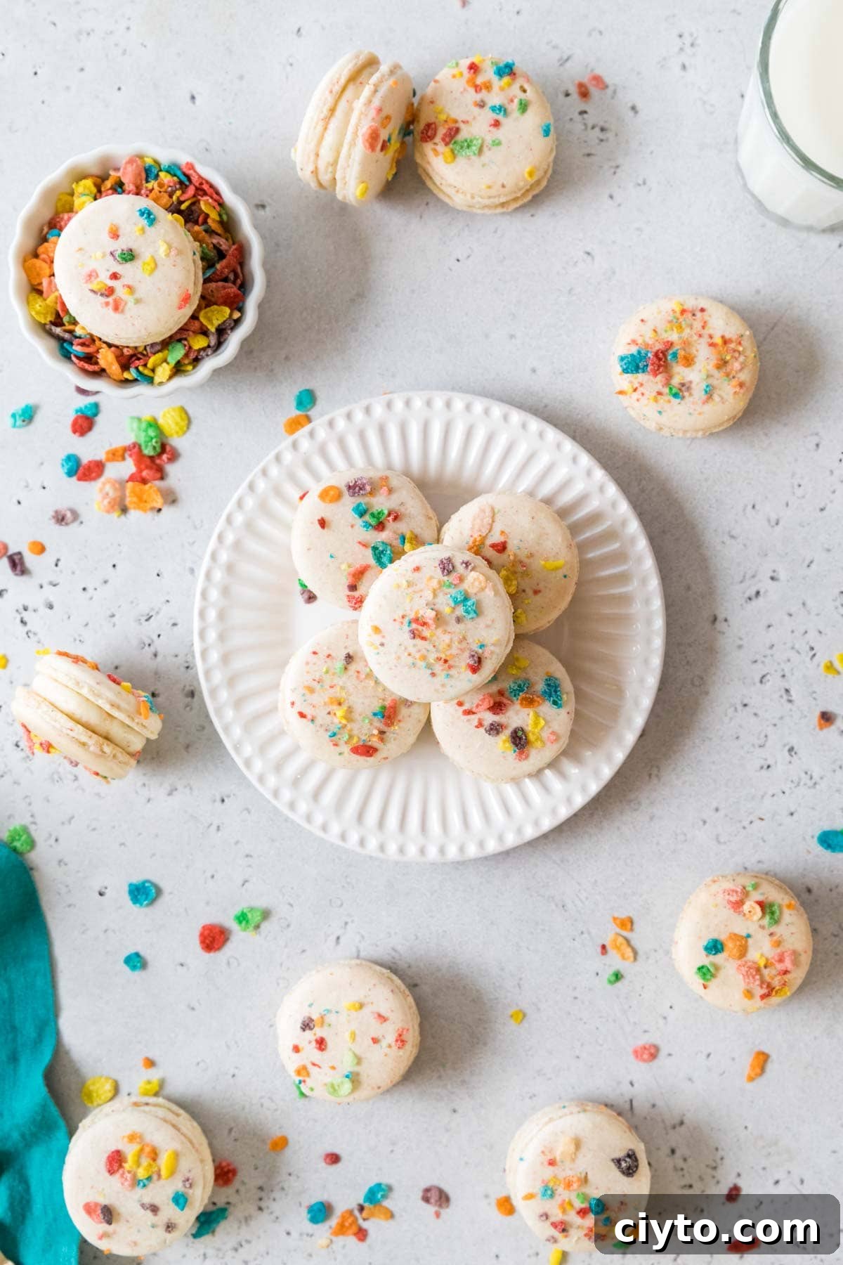 Overhead view of a plate with three macarons made with fruity pebbles arranged on top.