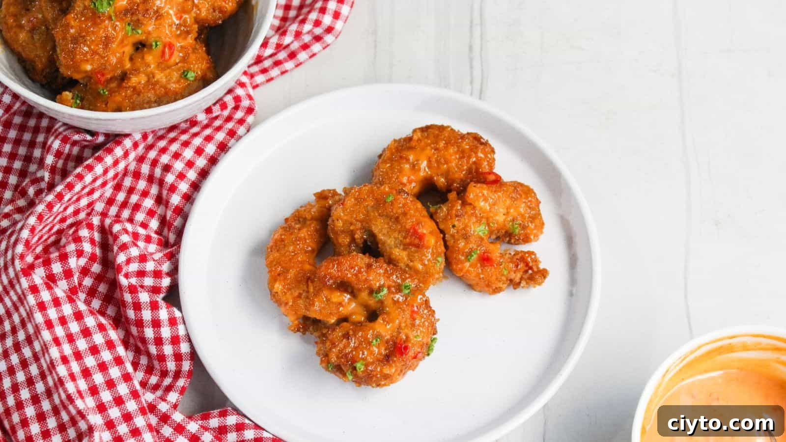 Fried shrimp on a plate next to a bowl of sauce.