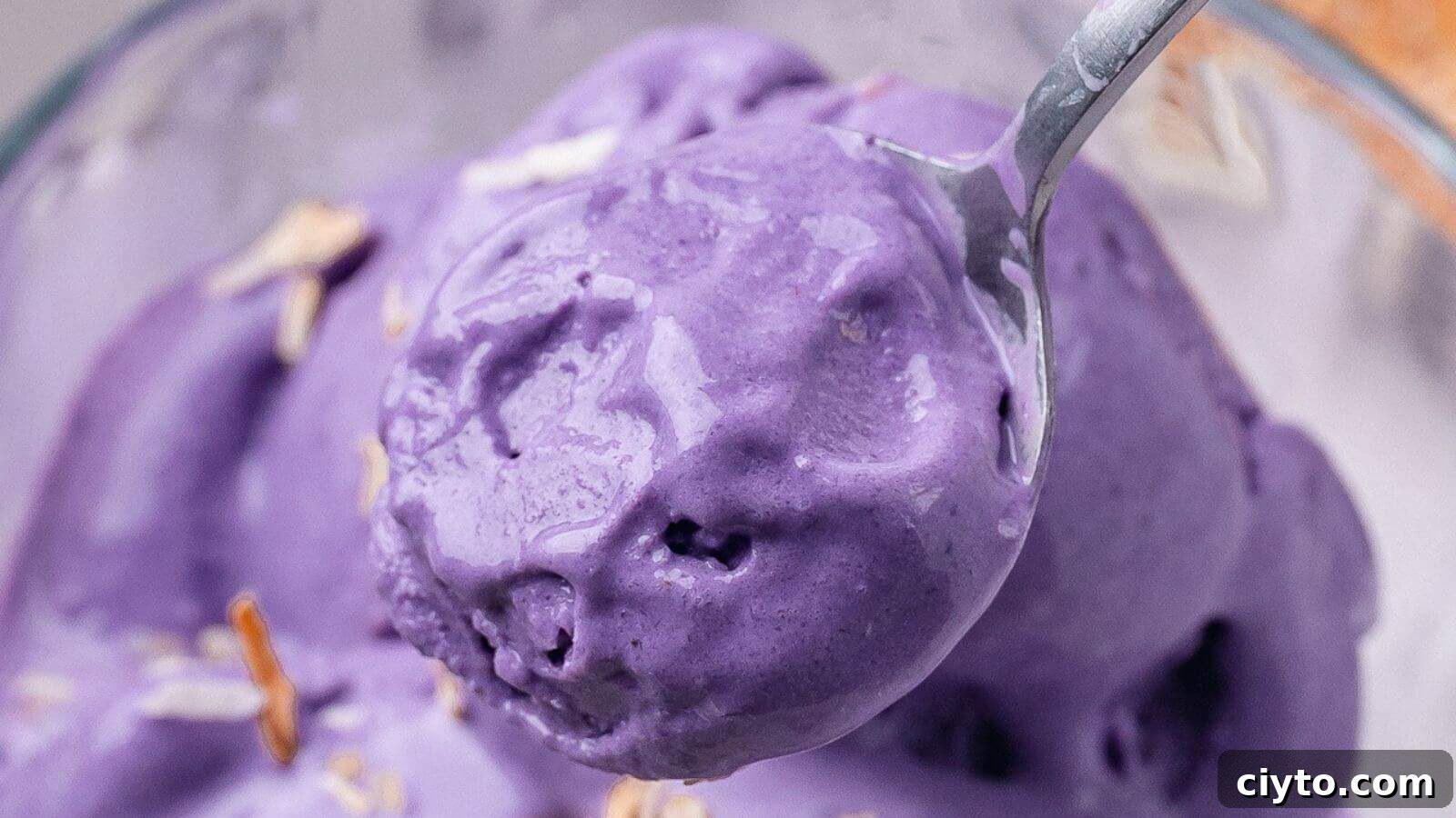 A close-up of purple ice cream in a bowl, with a spoon scooping out a portion.