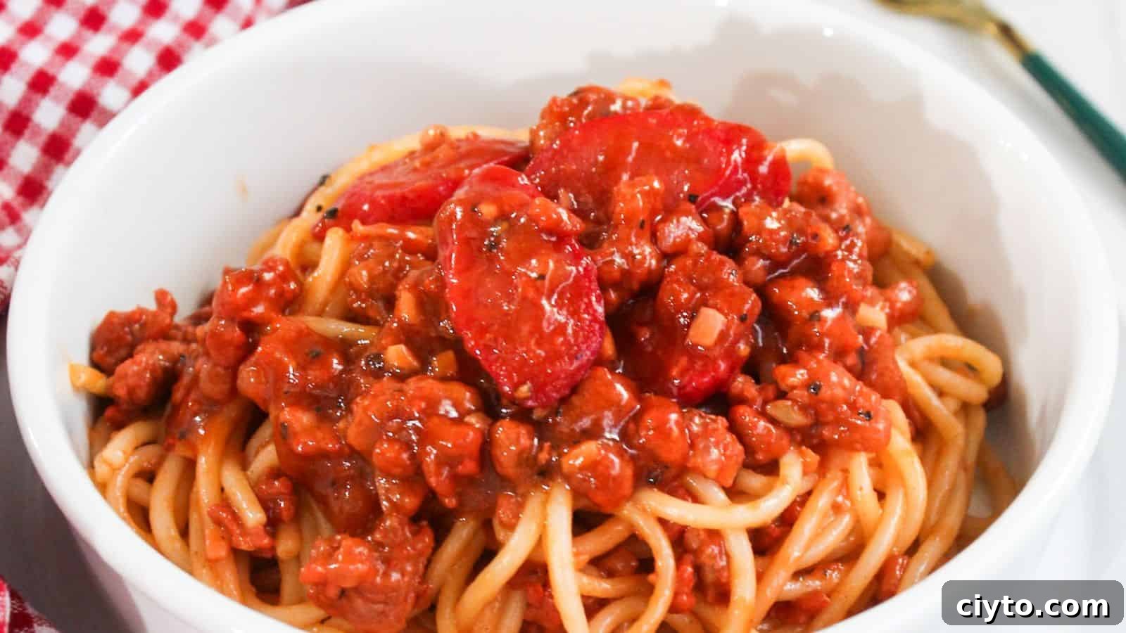 A bowl of spaghetti topped with a rich meat sauce placed on a red and white checkered tablecloth.