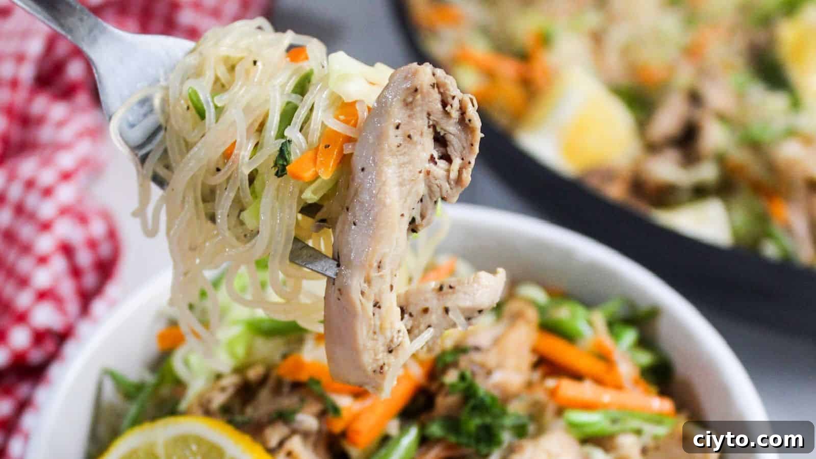 A fork lifting a portion of chicken and noodles from a bowl of stir-fry.