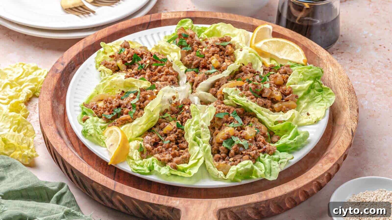 A plate of lettuce wraps filled with seasoned minced meat and garnished with herbs, served with lemon wedges on a wooden tray.