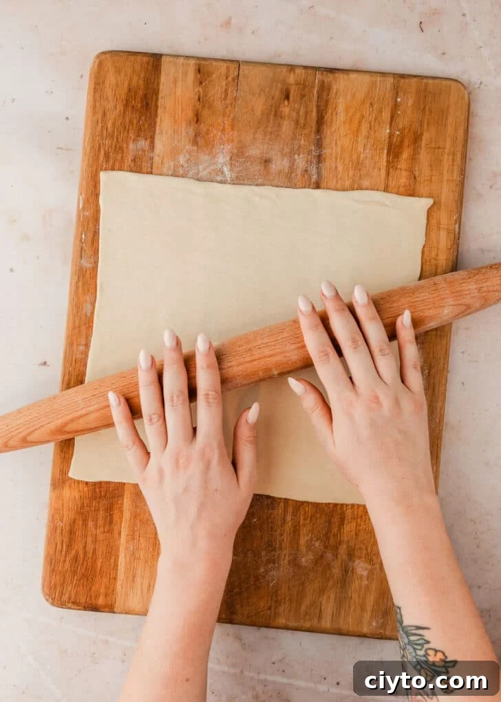 3-Ingredient Brie and Jam Puff Pastry Bites 4 Hands using a rolling pin to roll dough on a wood board.
