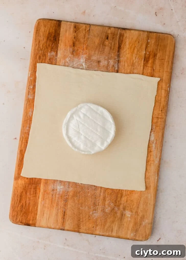 3-Ingredient Brie and Jam Puff Pastry Bites 5 A wheel of cheese in the middle of dough on a wood board.
