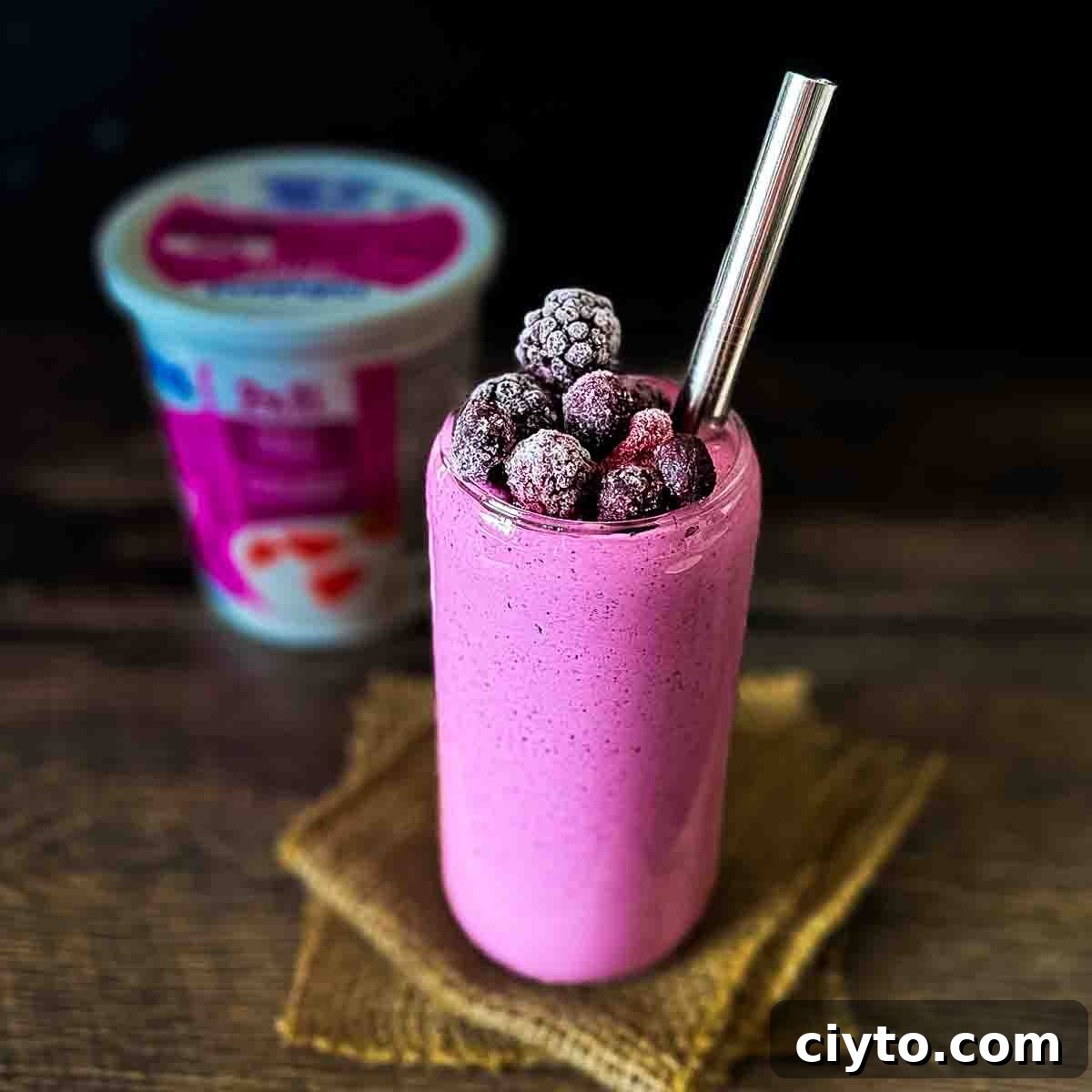 A glass filled with a purple berry smoothie with cottage cheese, with a container of cottage cheese in the background.