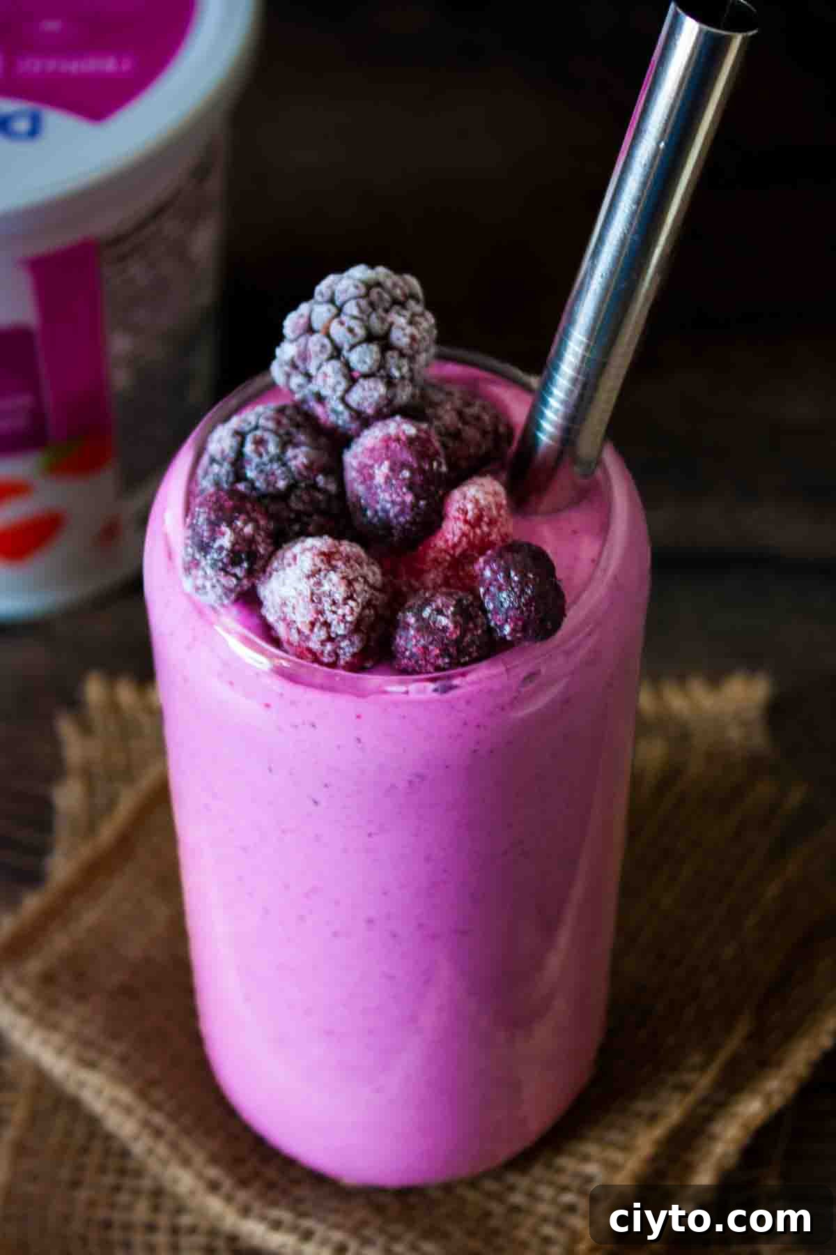 A tall glass with a metal straw showing the creamy texture of the berry smoothie made with cottage cheese.
